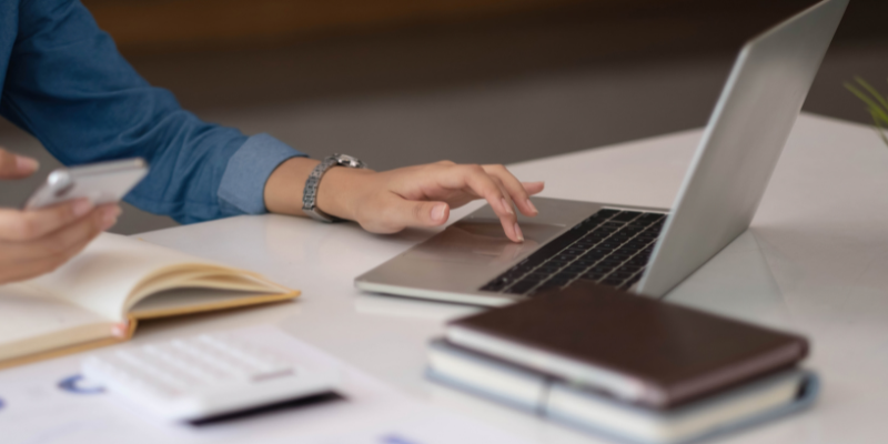 persona che tocca al trackpad del pc e che guarda il cellulare 