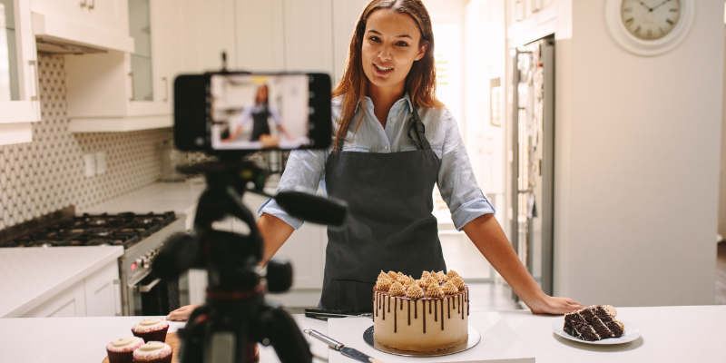 ragazza con capelli castani e grembiule nero che registra un video in cui mostra come preparare una torta con glassa al cioccolato